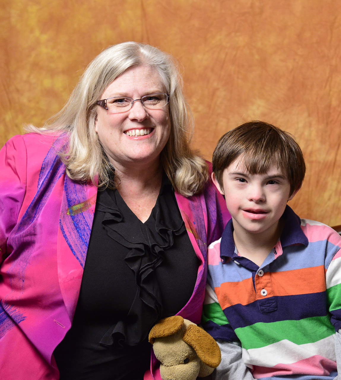 A woman and her son pose in front of an orange background.
